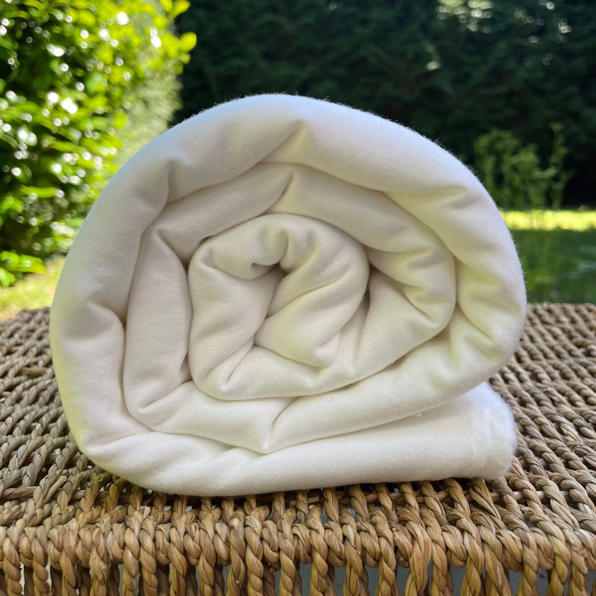 Rolled-up white bamboo fabric on a woven surface with greenery in the background