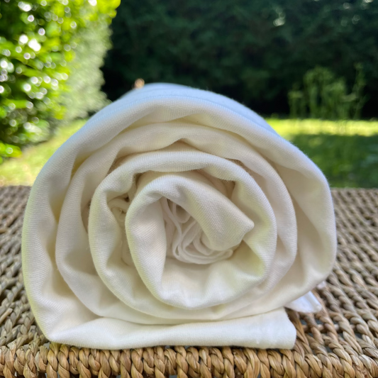 Rolled-up white terry fabric on a woven surface with greenery in the background